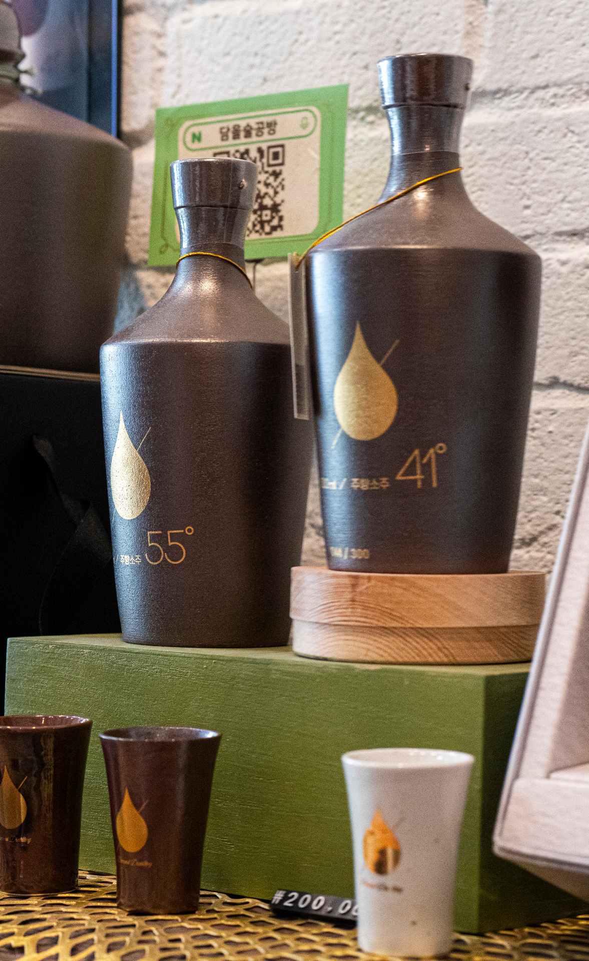 Modern craft soju bottles with golden droplet branding displayed at boutique distillery in Chungbuk