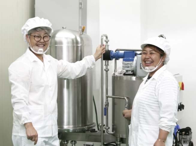 Joyful Korean distillery masters in white coats celebrating at modern soju production facility in Chungbuk